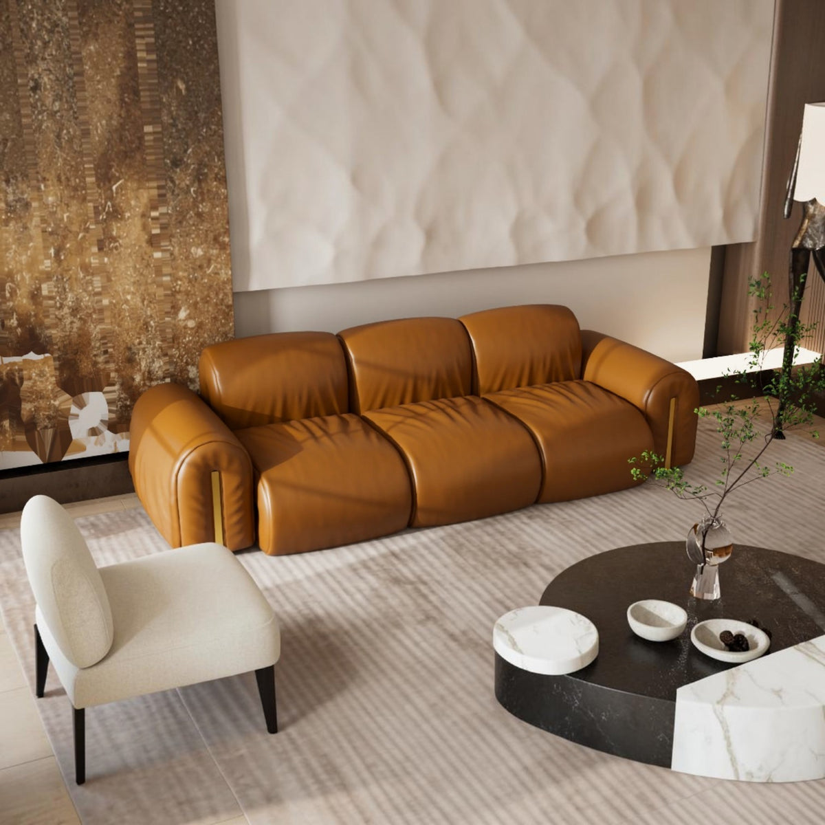A modern three-seater leather sofa in a warm camel brown color, styled in a contemporary living room with a cream accent chair, a round black and white coffee table, and a textured beige wall behind it.