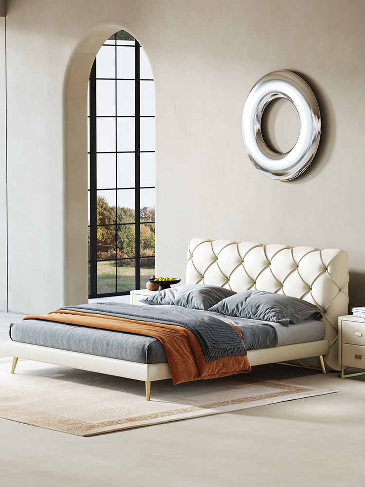 Modern bedroom with a tufted bed, large window, and decorative wall mirror.