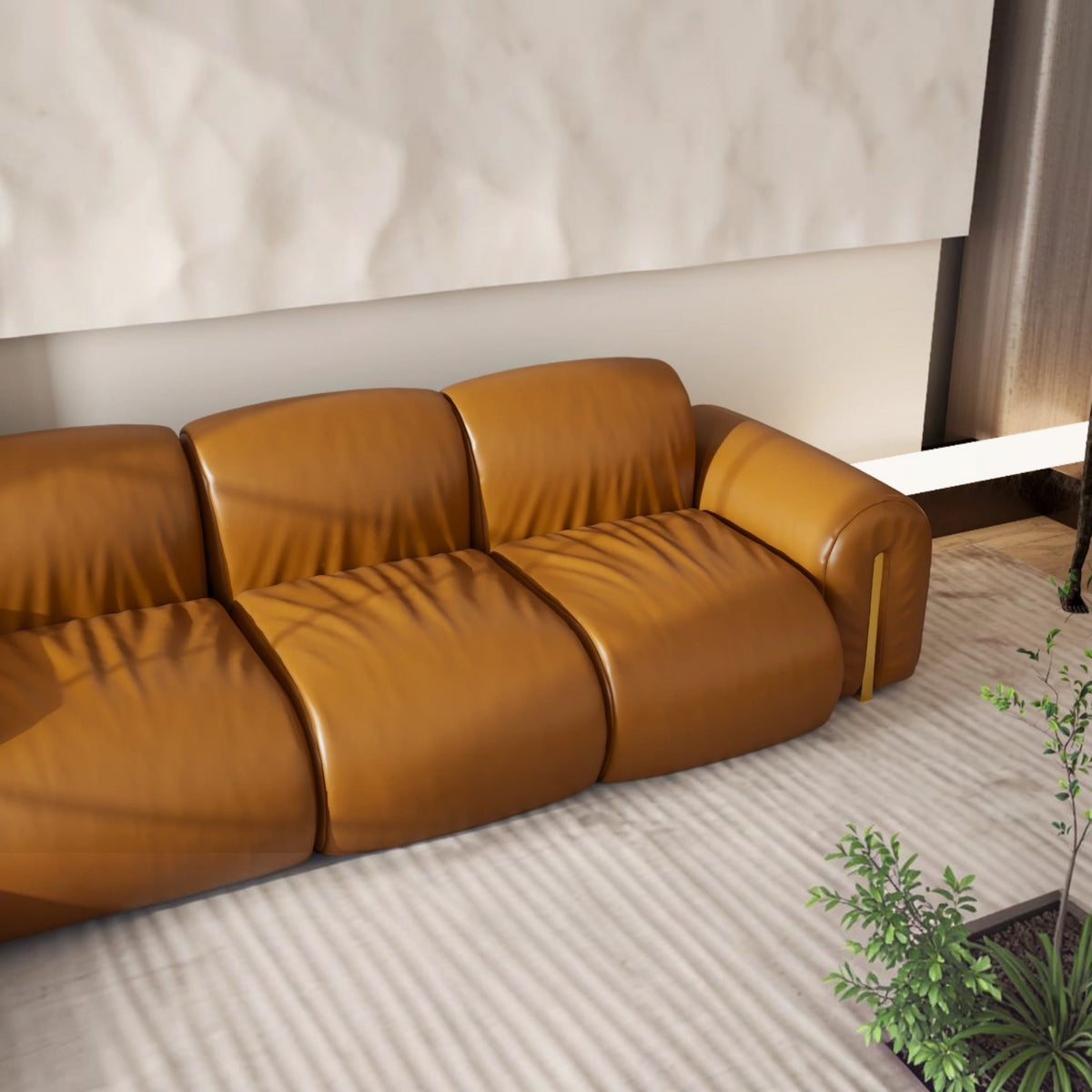 A modern three-seater sofa upholstered in warm camel-brown leather, shown in a minimalist living room setting with a textured light rug and a small potted plant.