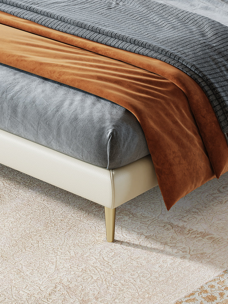 Close-up of a bed with brown and gray bedding on a beige carpet.