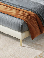 Close-up of a bed with brown and gray bedding on a beige carpet.
