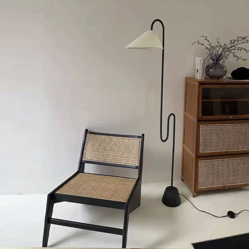 Chair with woven backrest and seat next to a floor lamp and wooden cabinet with wicker drawers.