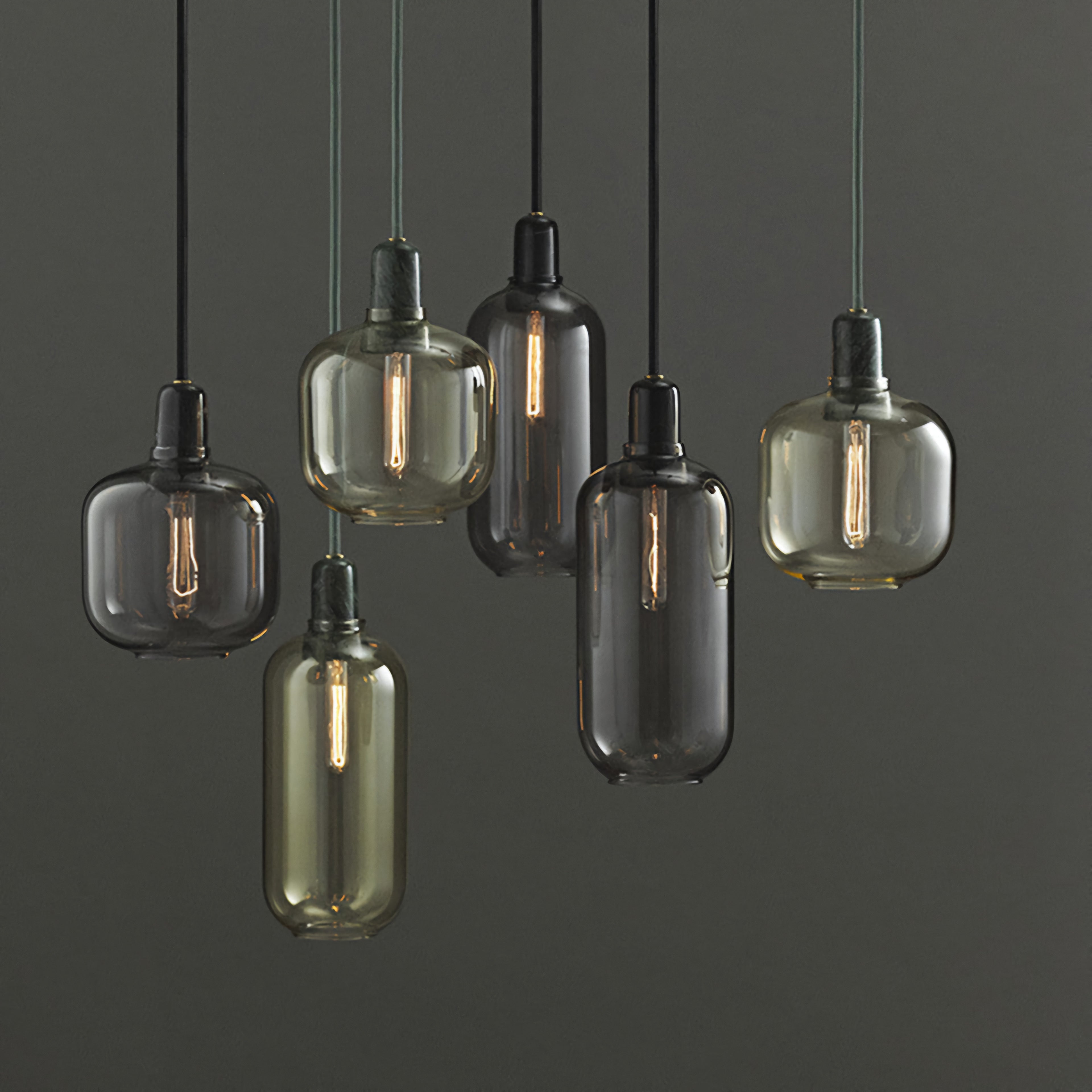 Six hanging pendant light fixtures with translucent smoked glass shades in smoky gray, amber, and dark charcoal tones, suspended against a dark gray background.