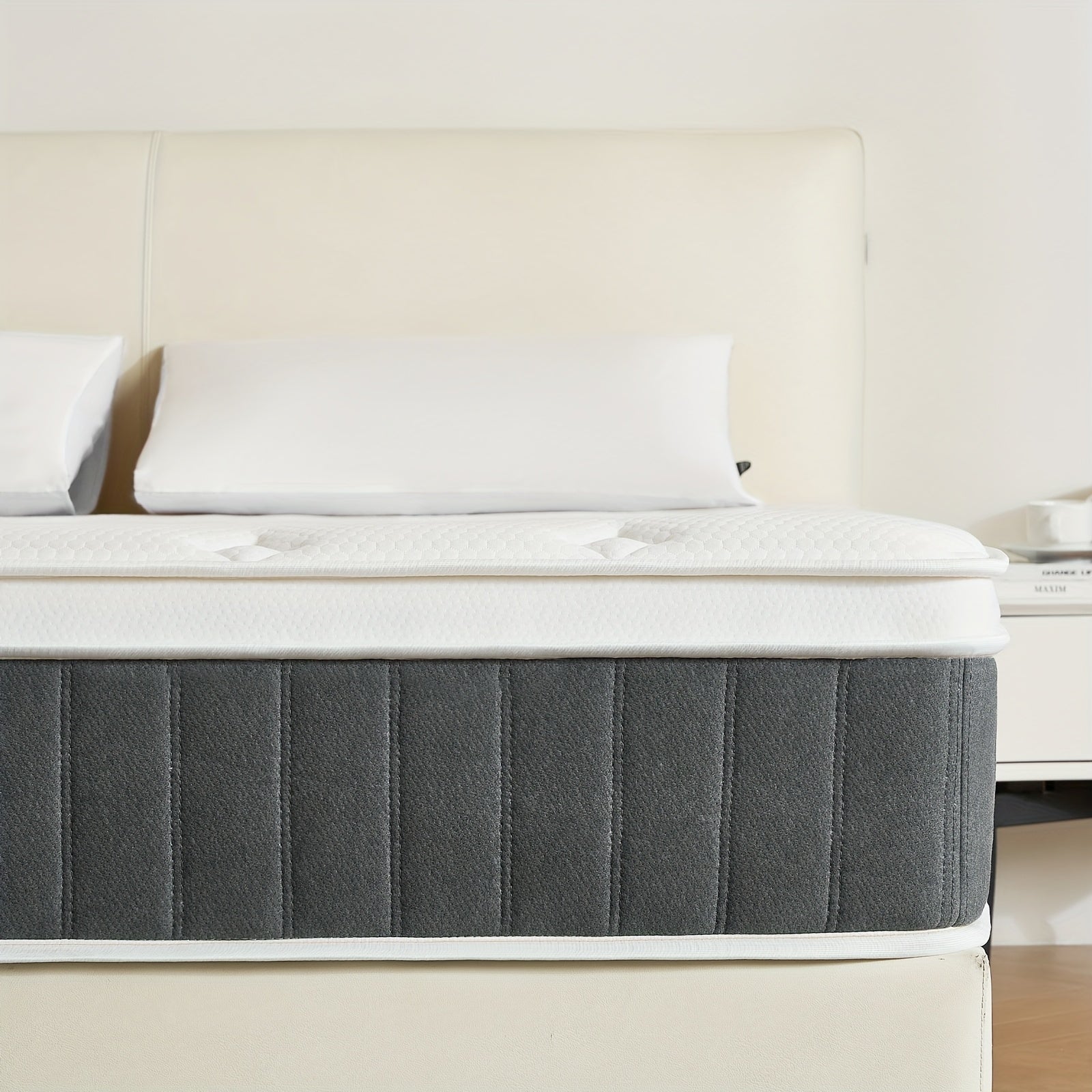 Gray mattress on a bed with white pillows and headboard in a room.