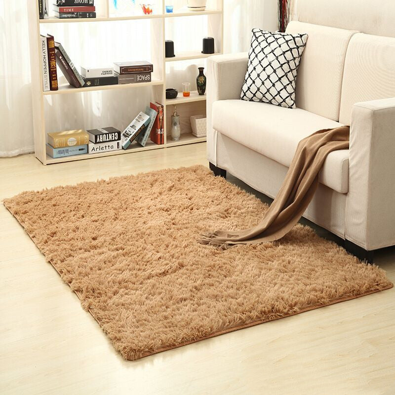 Beige rug on a wooden floor in a living room with a white sofa and bookshelf.