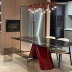 A modern dining table set in a kitchen, featuring a glossy black glass tabletop with gold stripes, a sculptural glossy red base, a matching glass bench, and two chairs with cream upholstery.
