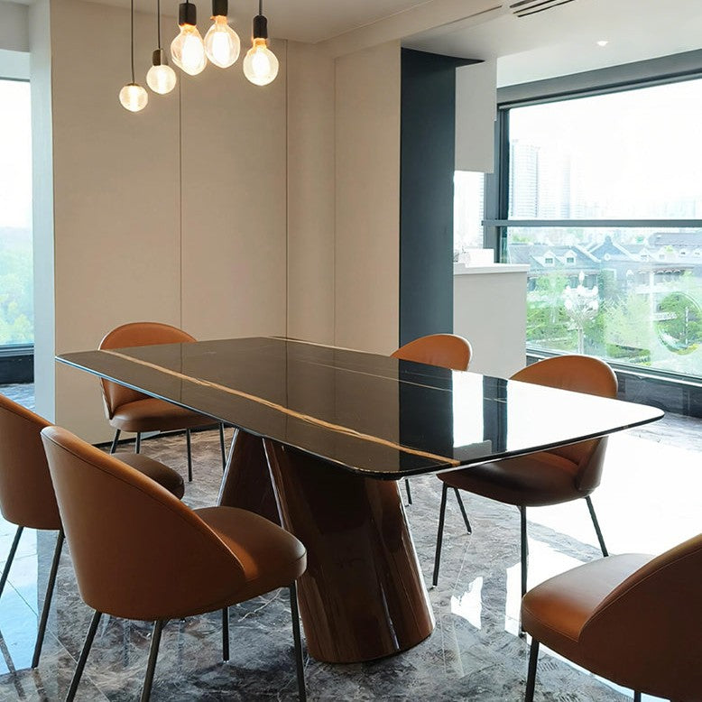 A modern dining room setup featuring a glossy black rectangular table with a sculptural metallic base, surrounded by six brown leather chairs. The room has beige walls, a hanging pendant light with six glowing bulbs, and large windows showing a city view.
