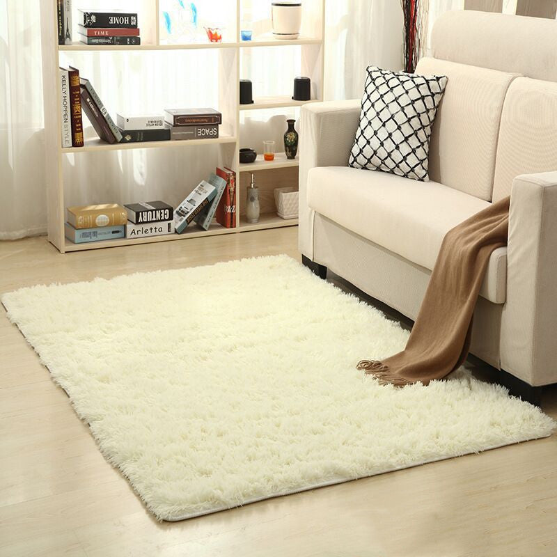 White fluffy rug on a wooden floor with a beige sofa and bookshelf in the background.