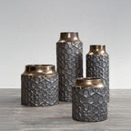 Set of four textured metal vases on a gray surface with a light gray background