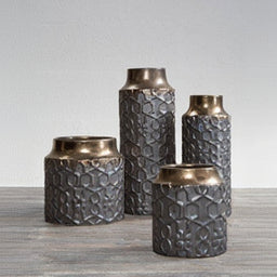 Set of four textured metal vases on a gray surface with a light gray background