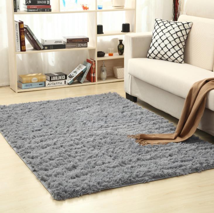 Gray rug on a light wood floor in a living room with a white sofa and bookshelf.