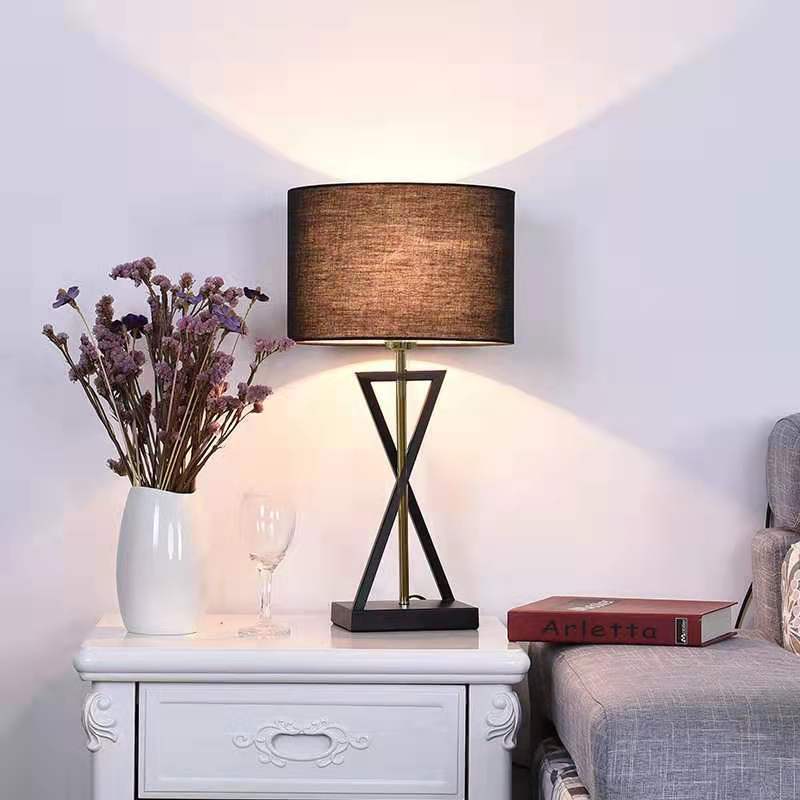 Table lamp on a nightstand with a vase of flowers and a book in a cozy living room setting.