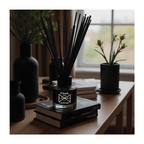 Black diffuser bottle labeled 'Dank Lavender' on books with plants in the background