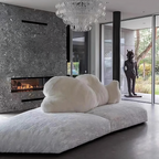 Modern living room with a large white cloud-shaped pillow on a sofa, a fireplace, and a chandelier.