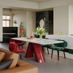 A modern dining room scene featuring a glossy red sculptural table with white top, surrounded by red and green velvet chairs in a contemporary interior.