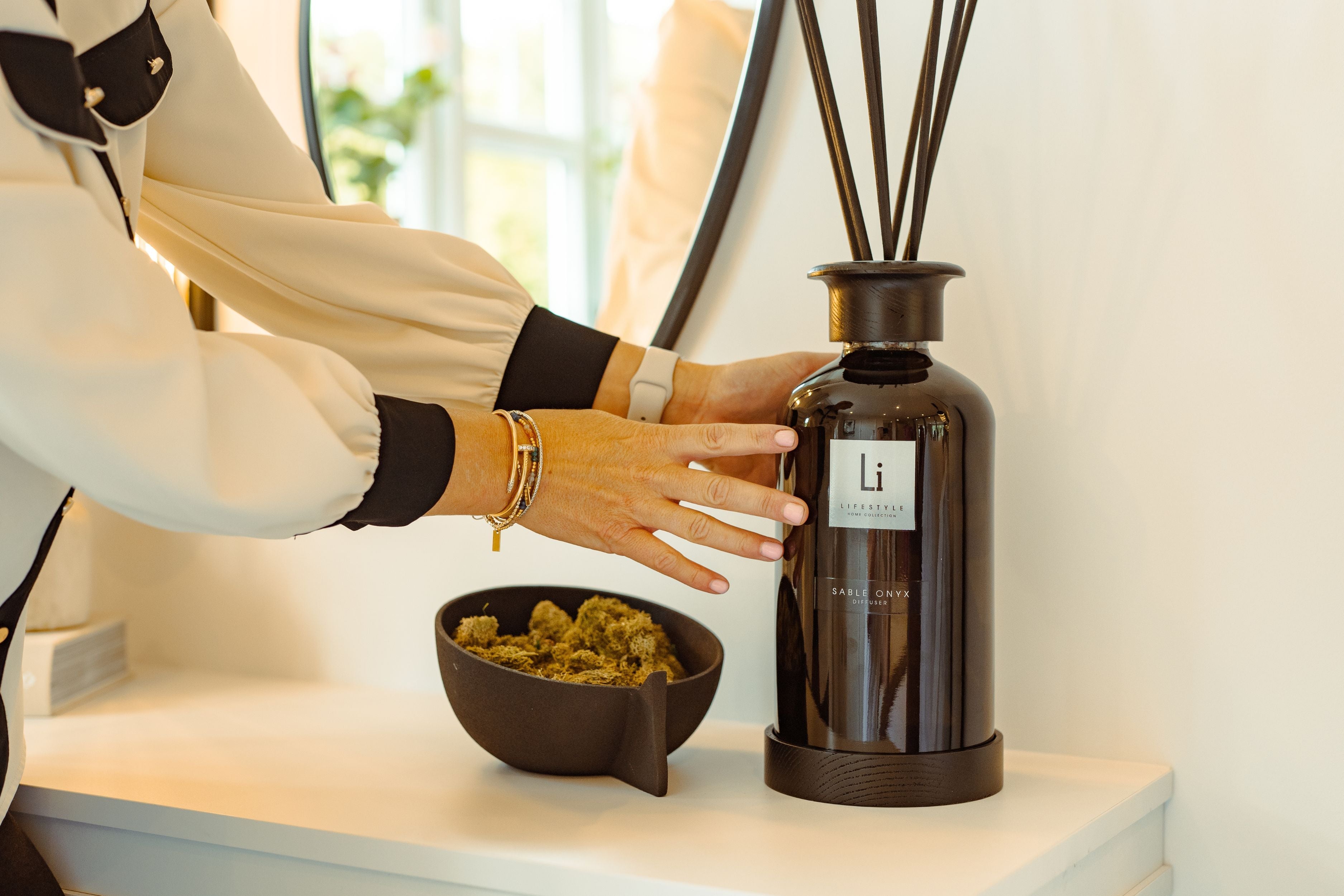 Person interacting with a diffuser and bowl on a shelf, with a brand label visible.