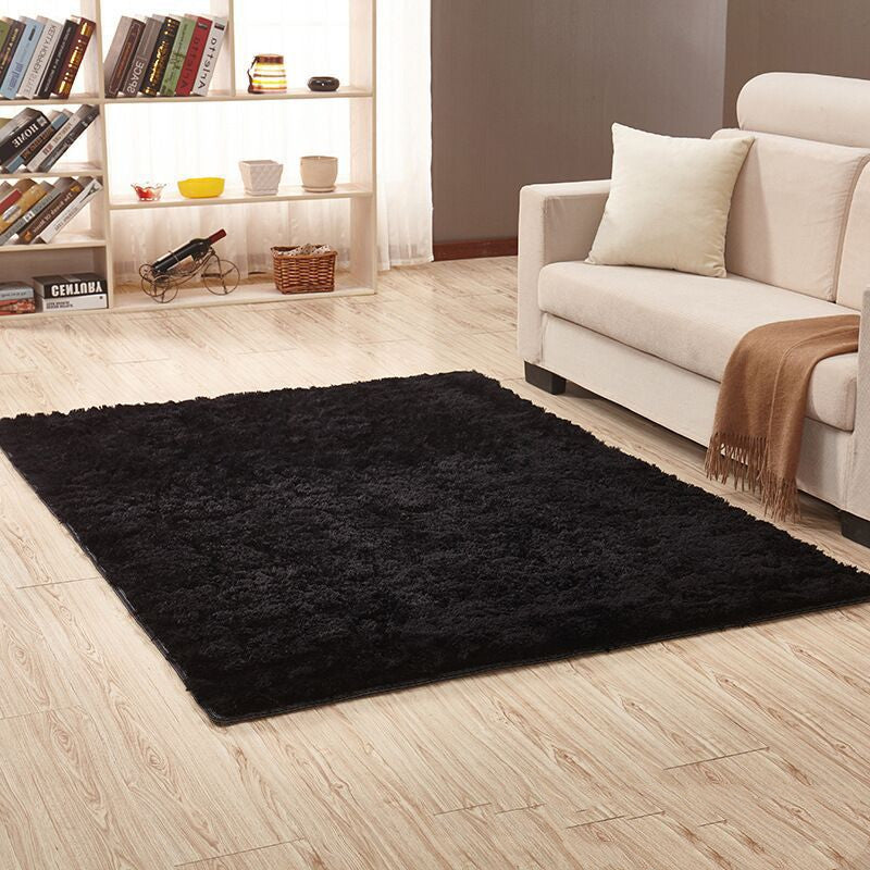 Black rug on a wooden floor in a living room with a beige sofa and bookshelf.