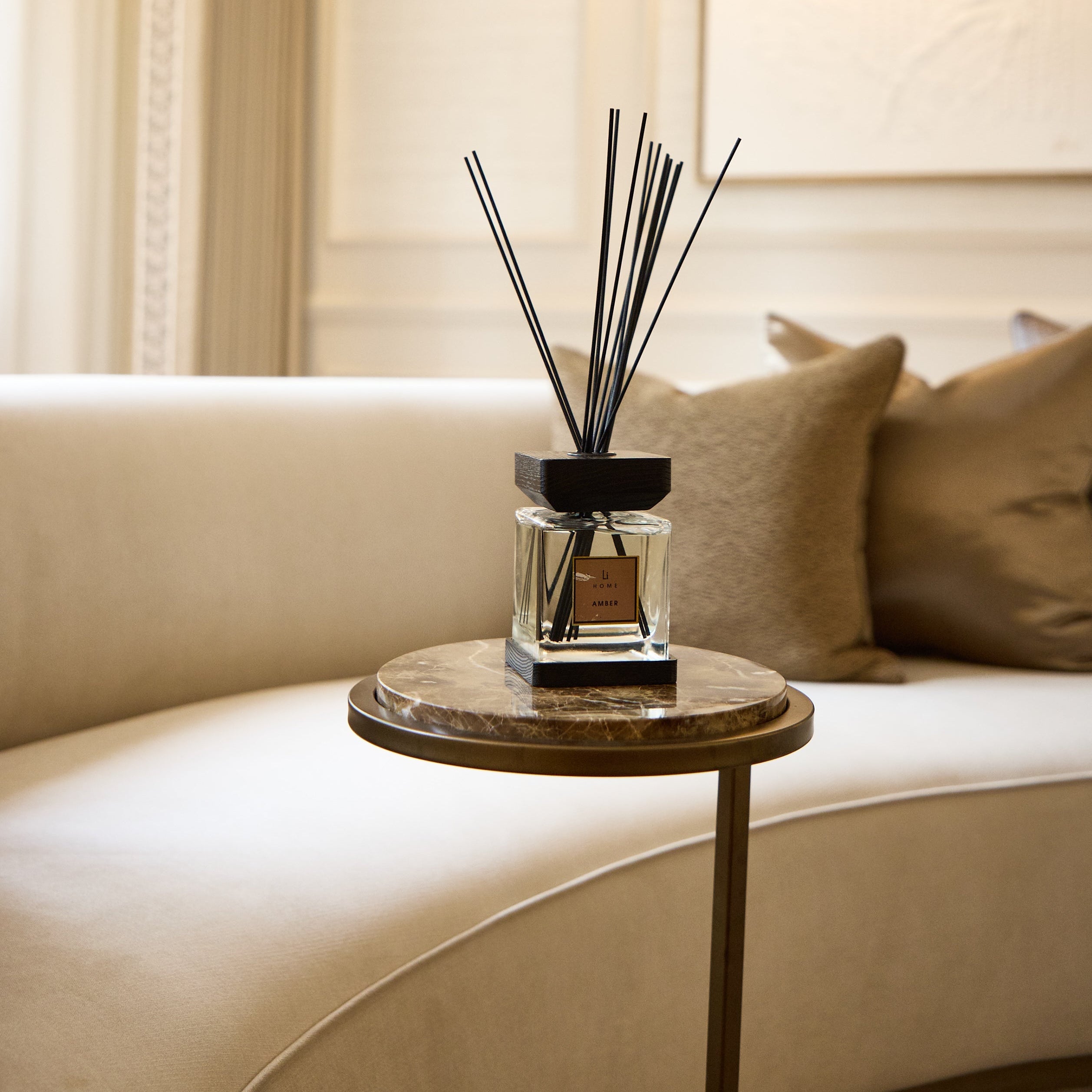 Reed diffuser on a small round table in a living room with beige sofa and curtains.