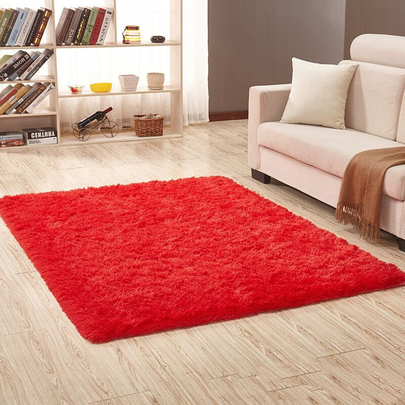 Red rug on a wooden floor in a living room with a beige sofa and bookshelf.