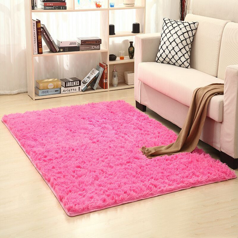 Pink rug on a light wood floor in a living room setting with a white sofa and bookshelf.