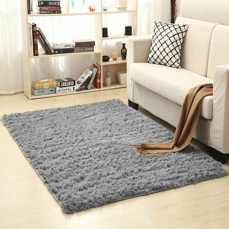 Gray rug on a wooden floor in a living room with a white sofa and bookshelf.