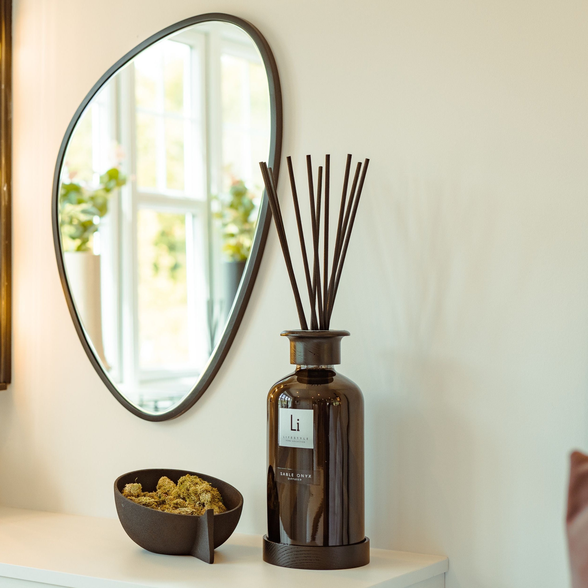 Decorative items on a shelf including a round mirror, diffuser, and small bowl.