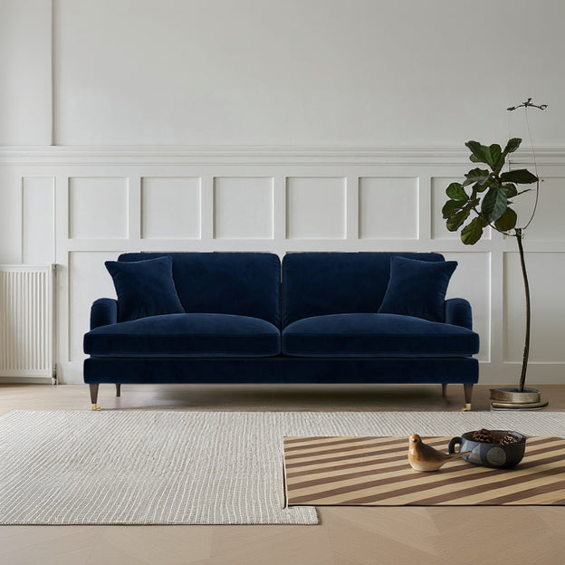 Navy blue velvet sofa in a room with white paneled walls and a plant.