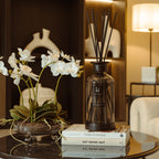 Decorative diffuser bottle on a table with flowers and books in a living room setting