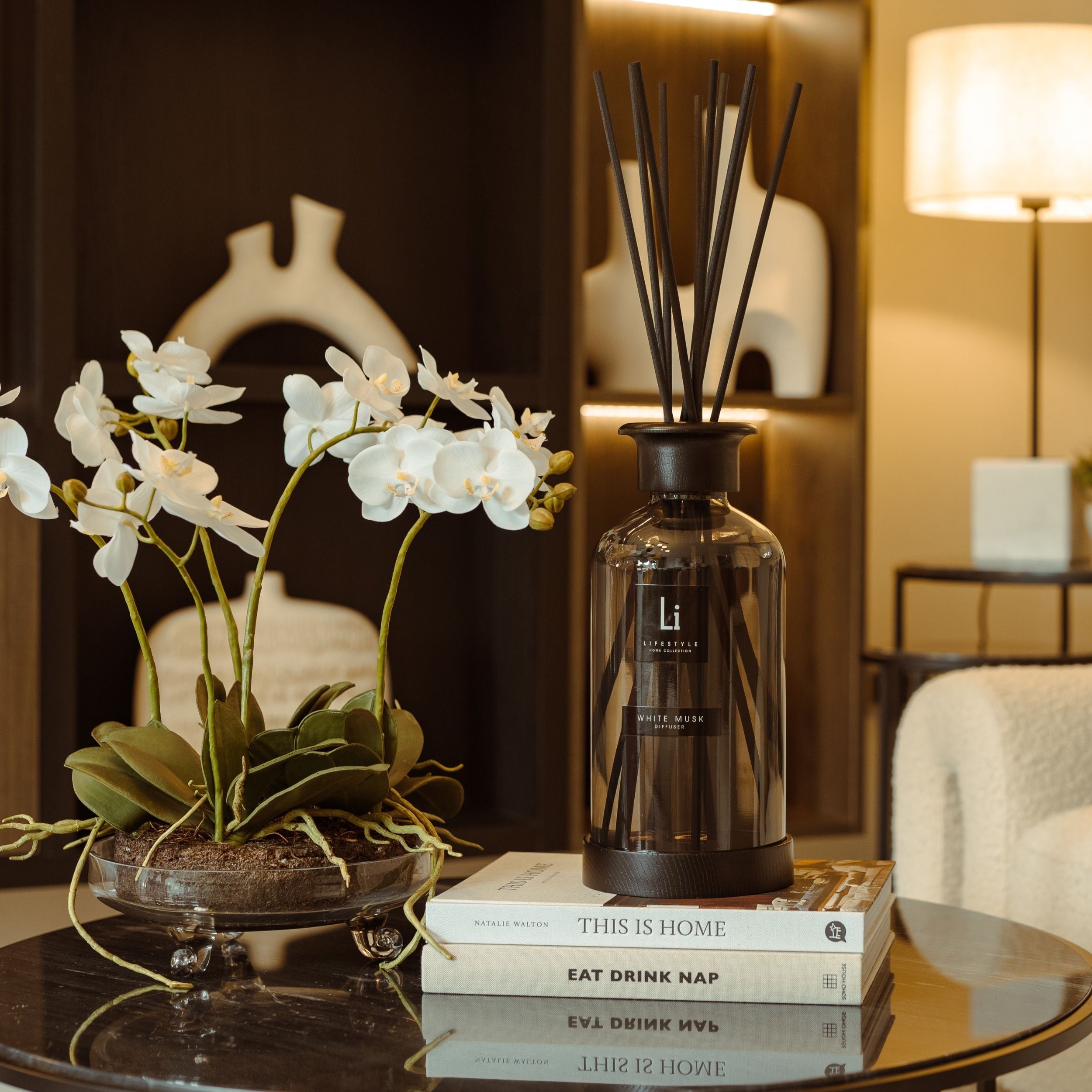 Decorative diffuser bottle on a table with flowers and books in a living room setting