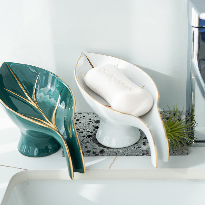 Teal leaf-shaped soap dish and white ceramic soap dish with soap on a bathroom counter.