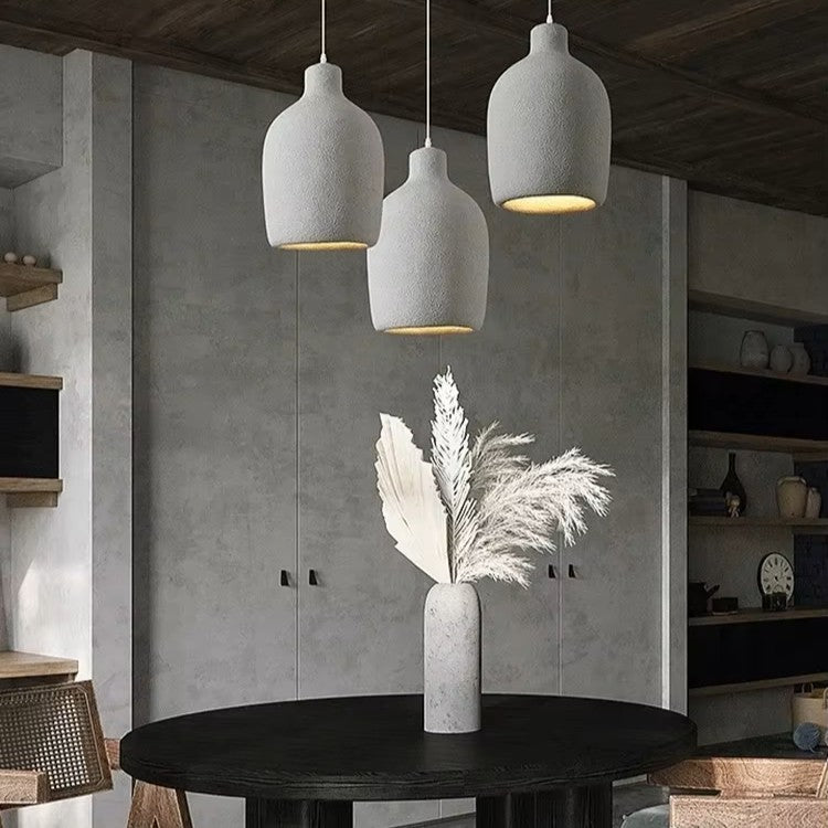 Modern interior with concrete pendant lights and a vase with dried plants on a table.