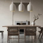 Dining area with a wooden table and chairs, featuring pendant lights and a vase with branches.