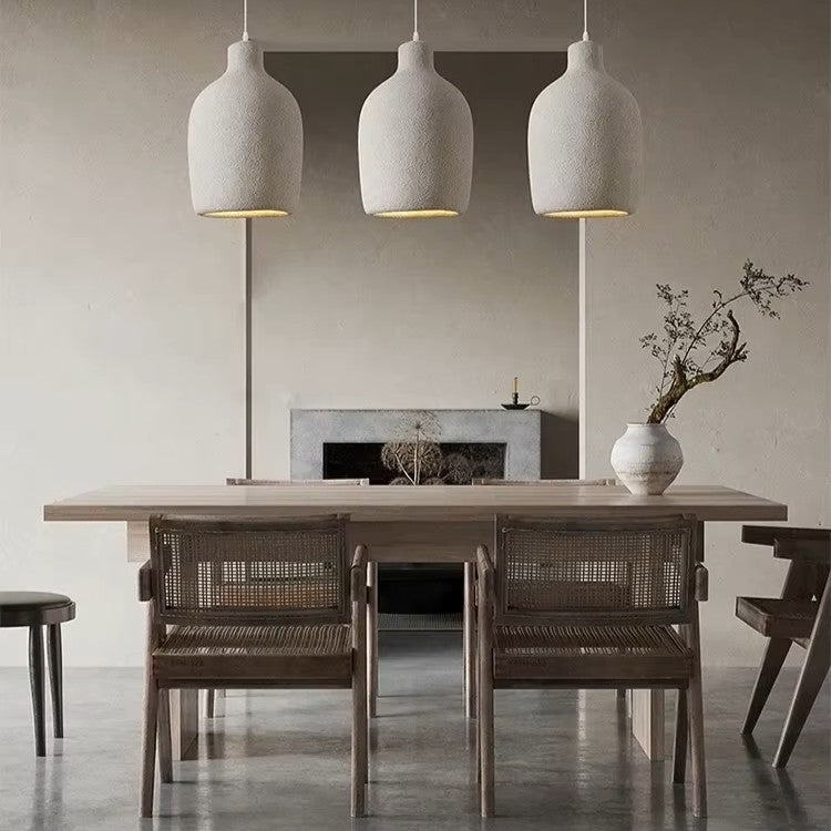 Dining area with a wooden table and chairs, featuring pendant lights and a vase with branches.