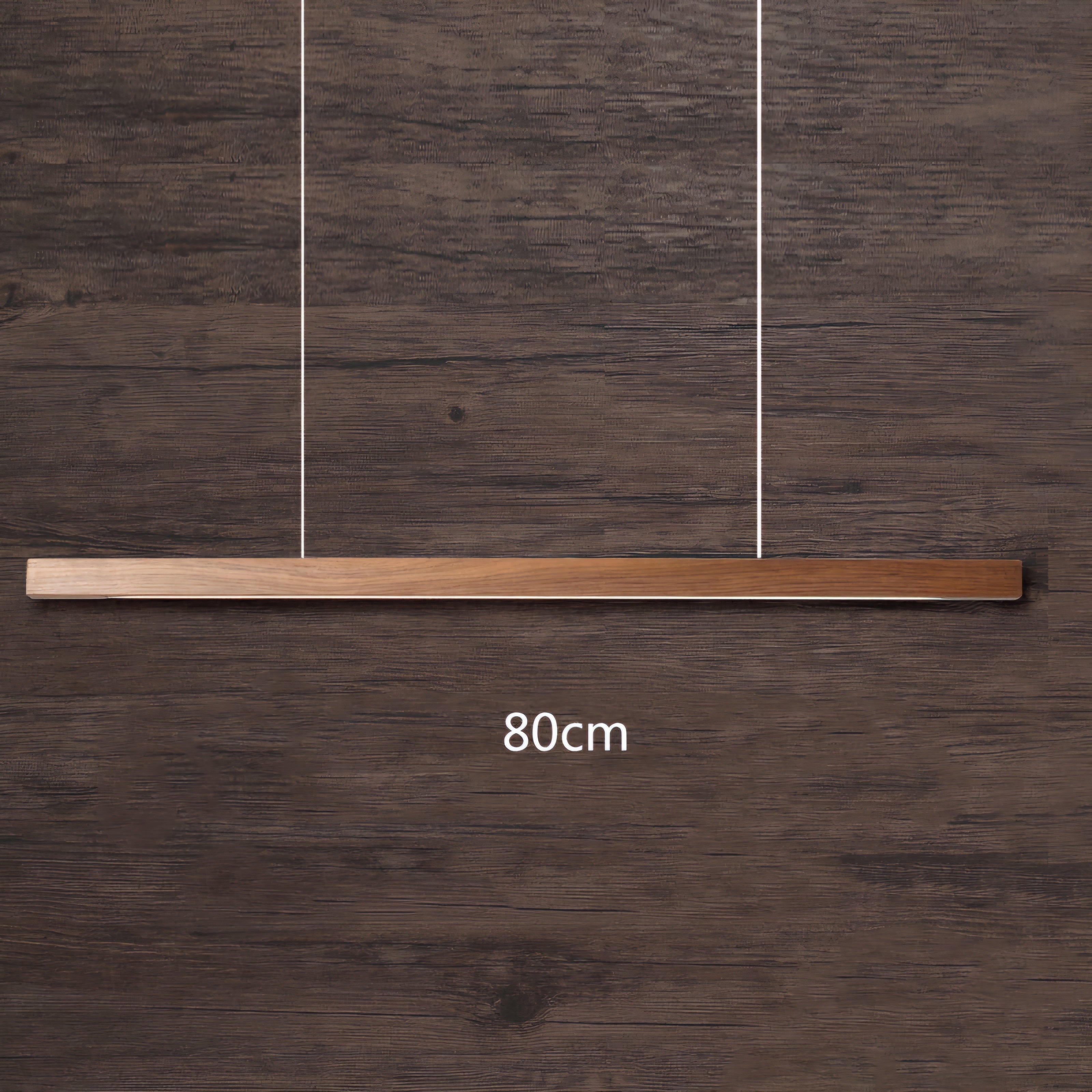 A modern linear pendant light with a brushed brass or bronze horizontal bar suspended by two thin vertical wires, shown against a dark brown wood plank background with an '80cm' size overlay.