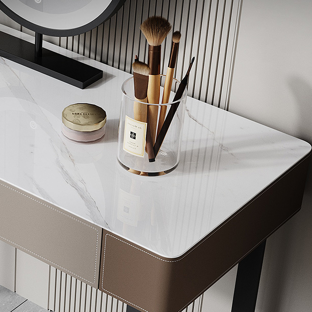 Dressing table with makeup brushes in a glass holder and a jar on a marble surface.