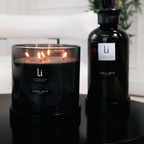Black candle and bottle with 'Li' branding on a reflective surface.