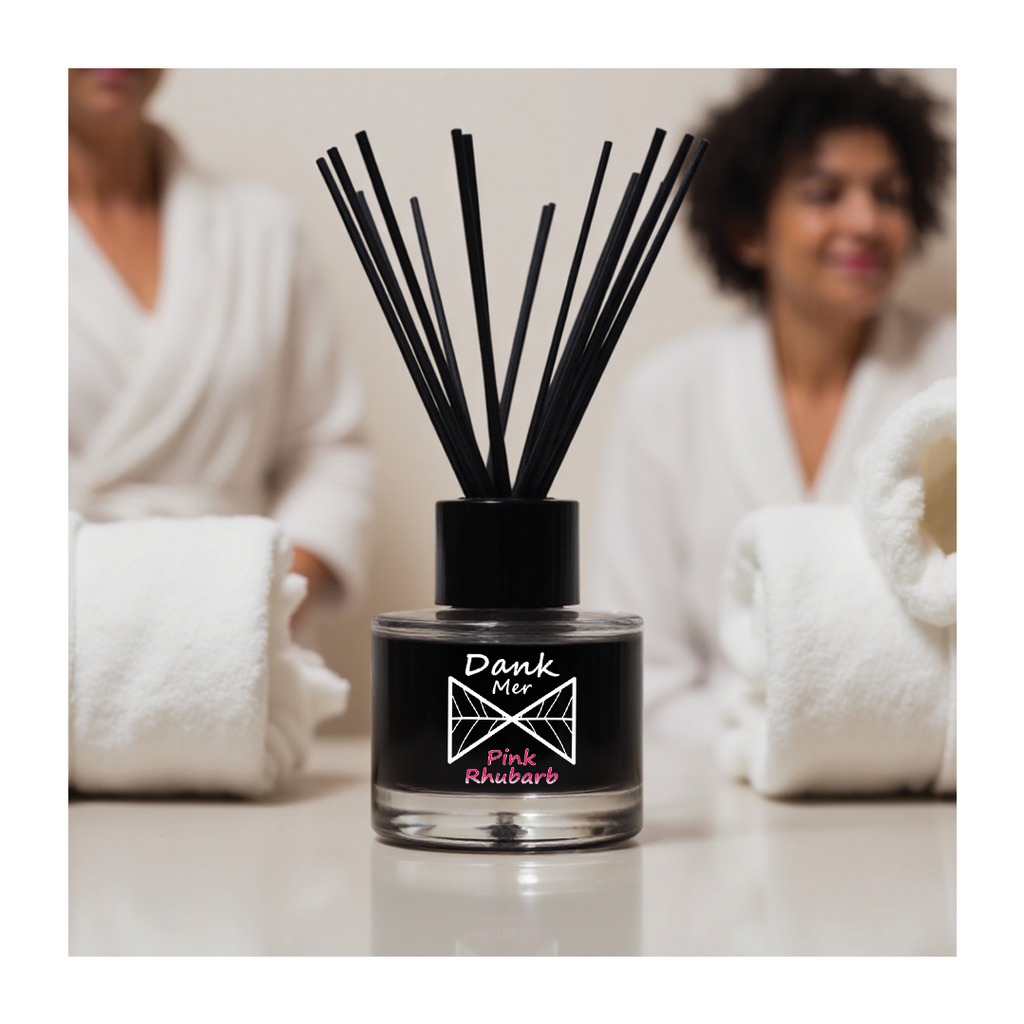 Black diffuser bottle with sticks labeled 'Dank Mer Pink Rhubarb' on a blurred background of people in robes.