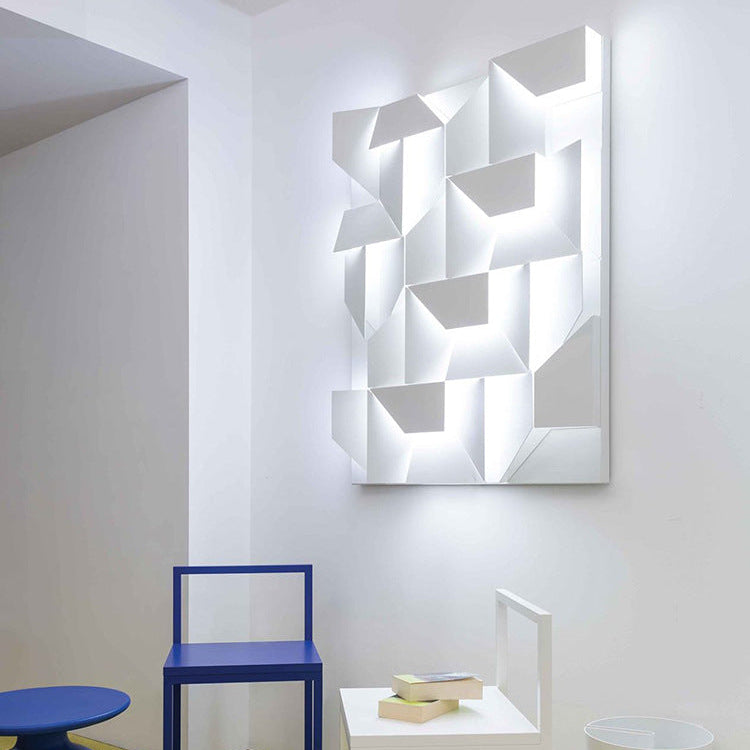 Modern wall art with geometric design on a white wall, featuring a blue chair and small table in the foreground.