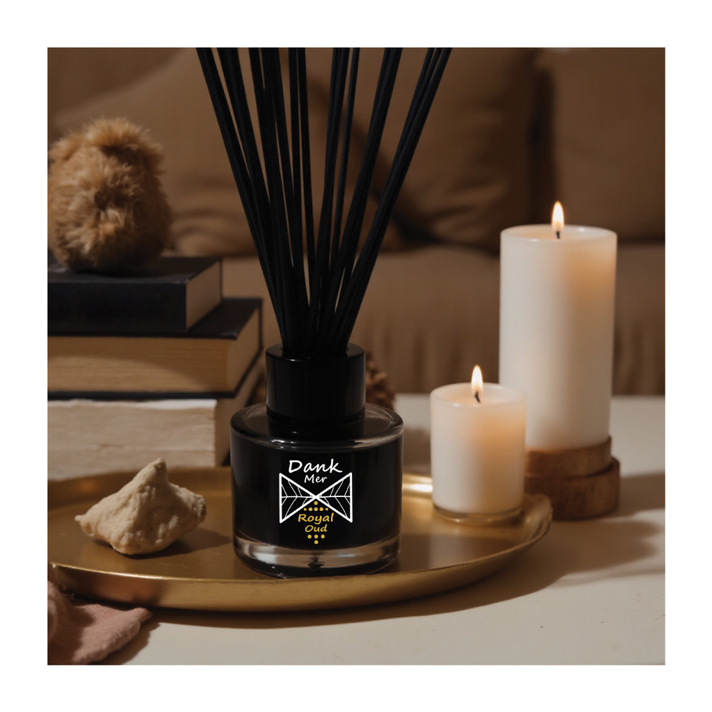 Black diffuser with reeds on a tray next to two white candles in a cozy setting.