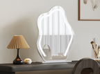 Decorative mirror with wavy design on a wooden surface with a lamp and other items.