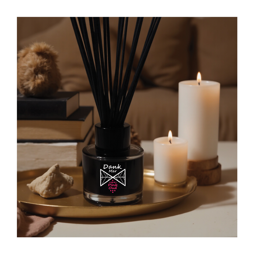 Black diffuser with sticks on a tray next to two white candles in a cozy indoor setting.