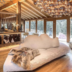 Modern living room with a cloud-shaped sofa, large chandelier, and wooden interior.