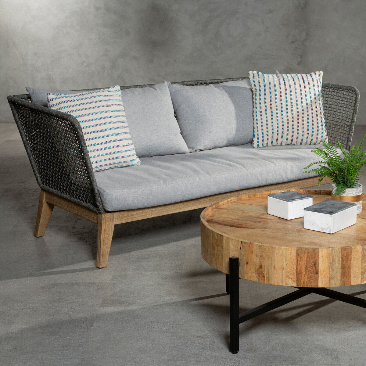 Gray sofa with striped cushions and a wooden coffee table on a concrete floor.