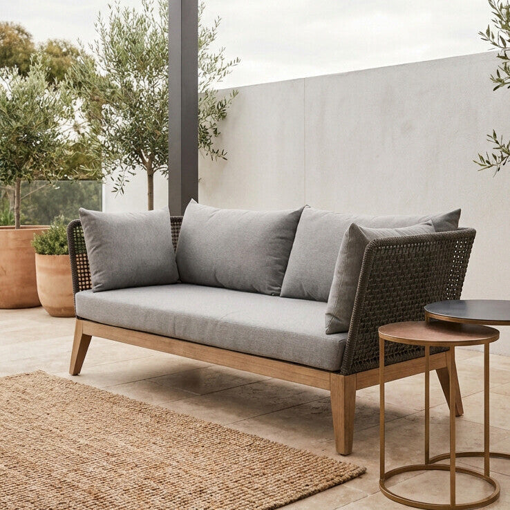 Outdoor sofa with gray cushions on a patio with plants and a wall in the background
