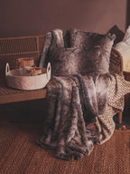 Brown textured blanket draped over a wicker chair with a basket on a matching surface.