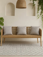 Wicker bench with gray cushions in a room with a patterned rug and wall decorations.