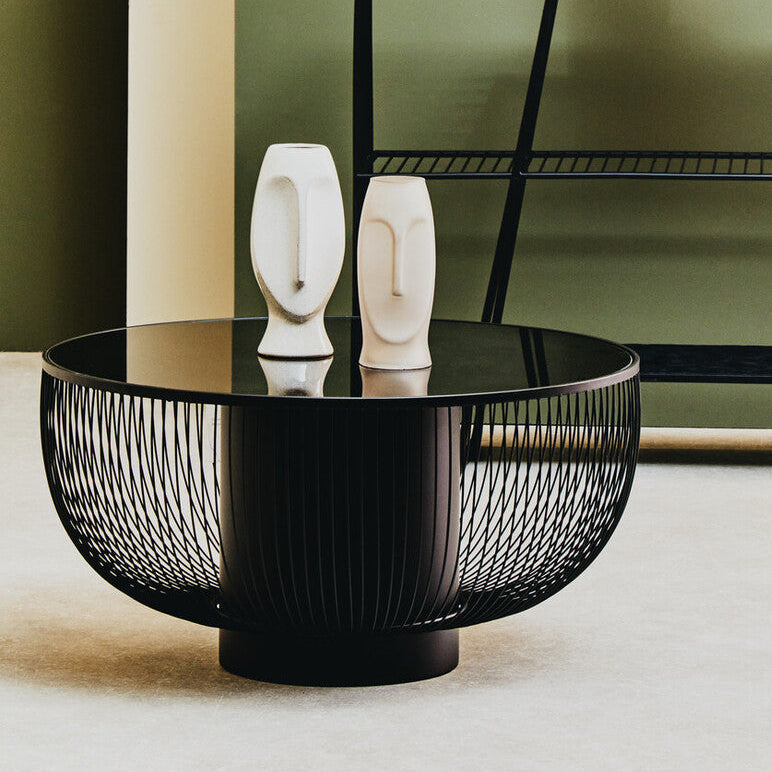 Black wire coffee table with two white ceramic face sculptures on a neutral background