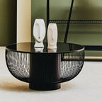 Black wire coffee table with two white ceramic face sculptures on a neutral background