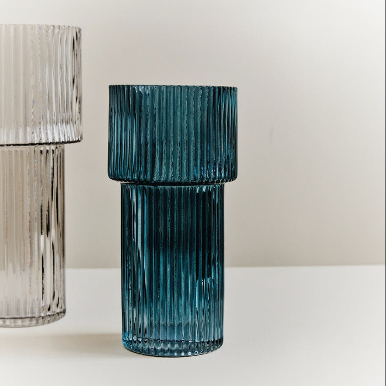Blue ribbed glass vase on a white surface with a neutral background