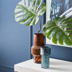Two vases on a white surface with a plant against a blue wall